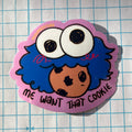 Sticker with a cartoon character and text 'Me want that cookie' on a grid background