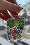 Hand holding a keychain with a colorful design of a green character and text.