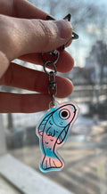 Hand holding a keychain with a fish design in front of a window
