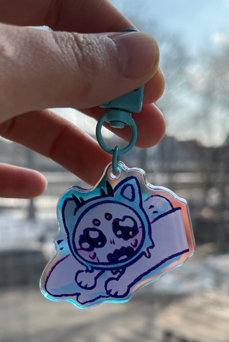 Hand holding a cartoon character keychain with a blurred cityscape in the background