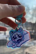 Hand holding a cartoon character keychain with a blurred cityscape in the background