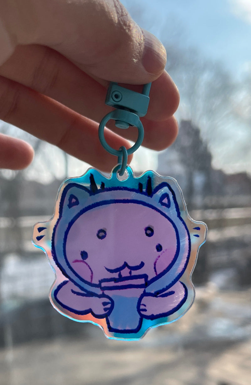 Hand holding a cartoon cat-shaped keychain with a blurred cityscape in the background