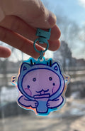 Hand holding a cartoon cat-shaped keychain with a blurred cityscape in the background