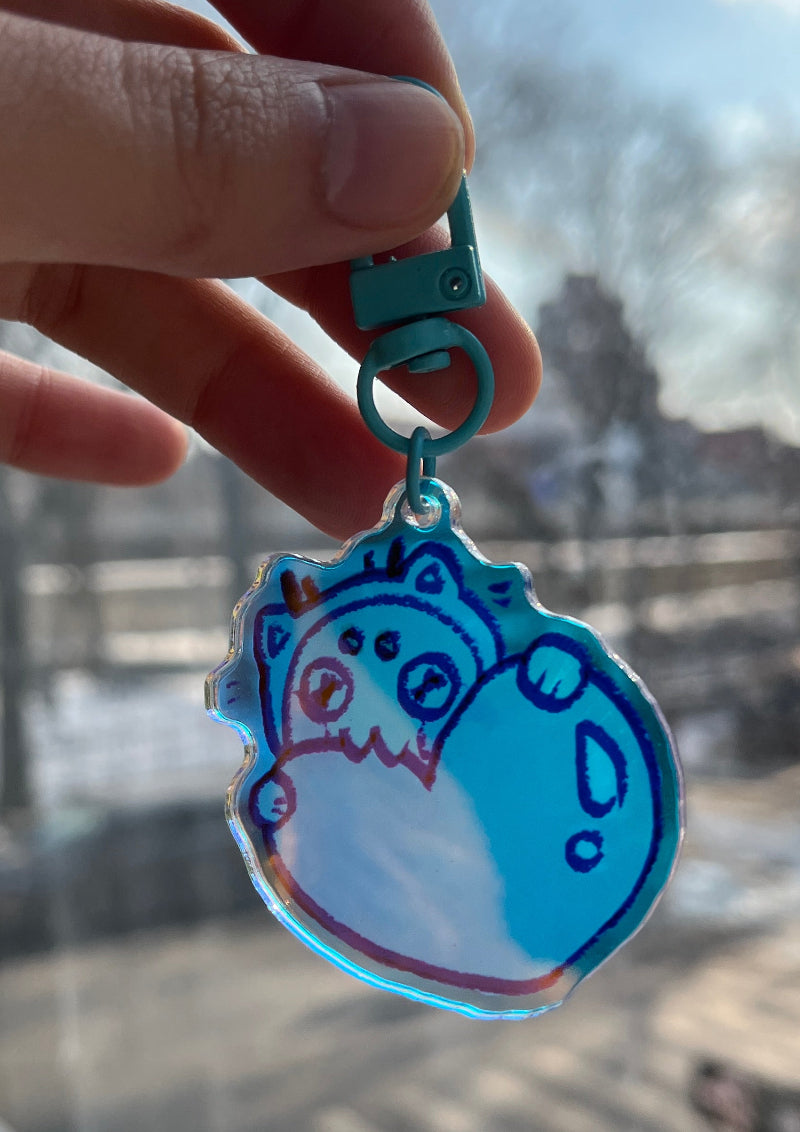 Hand holding a blue cartoon character keychain with a blurred cityscape in the background