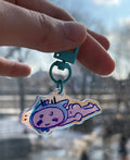 Hand holding a small colorful keychain with a character design, blurred cityscape in the background