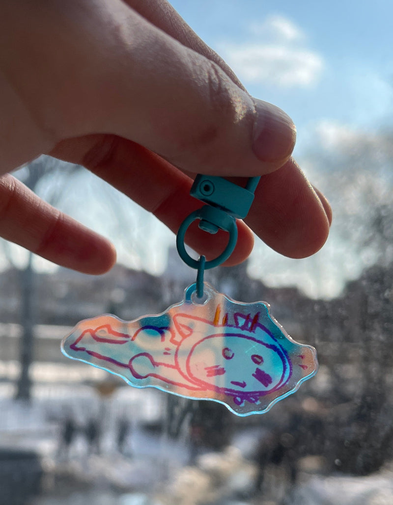 Hand holding a colorful keychain object with a cityscape in the background