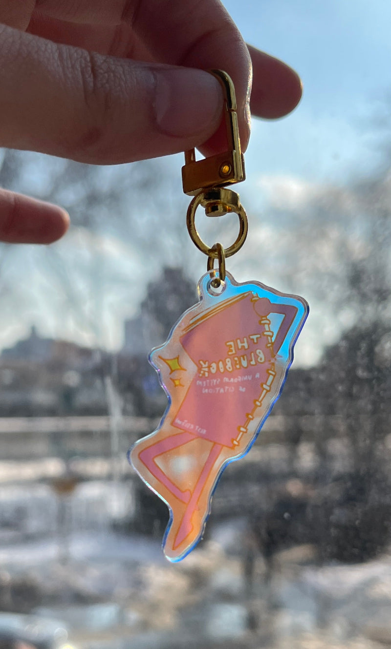 Hand holding a keychain with a colorful sticker in front of a blurred background