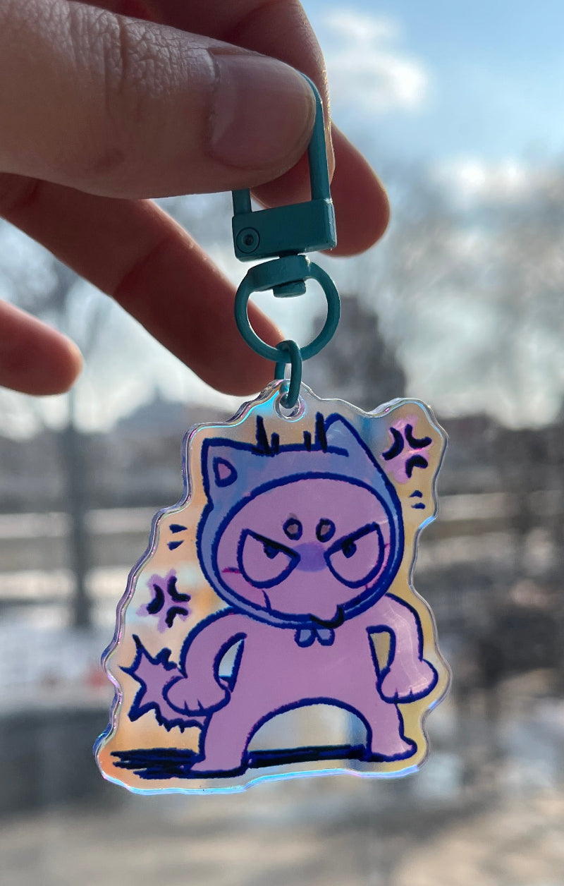 Hand holding a colorful keychain with a character design against a blurred background