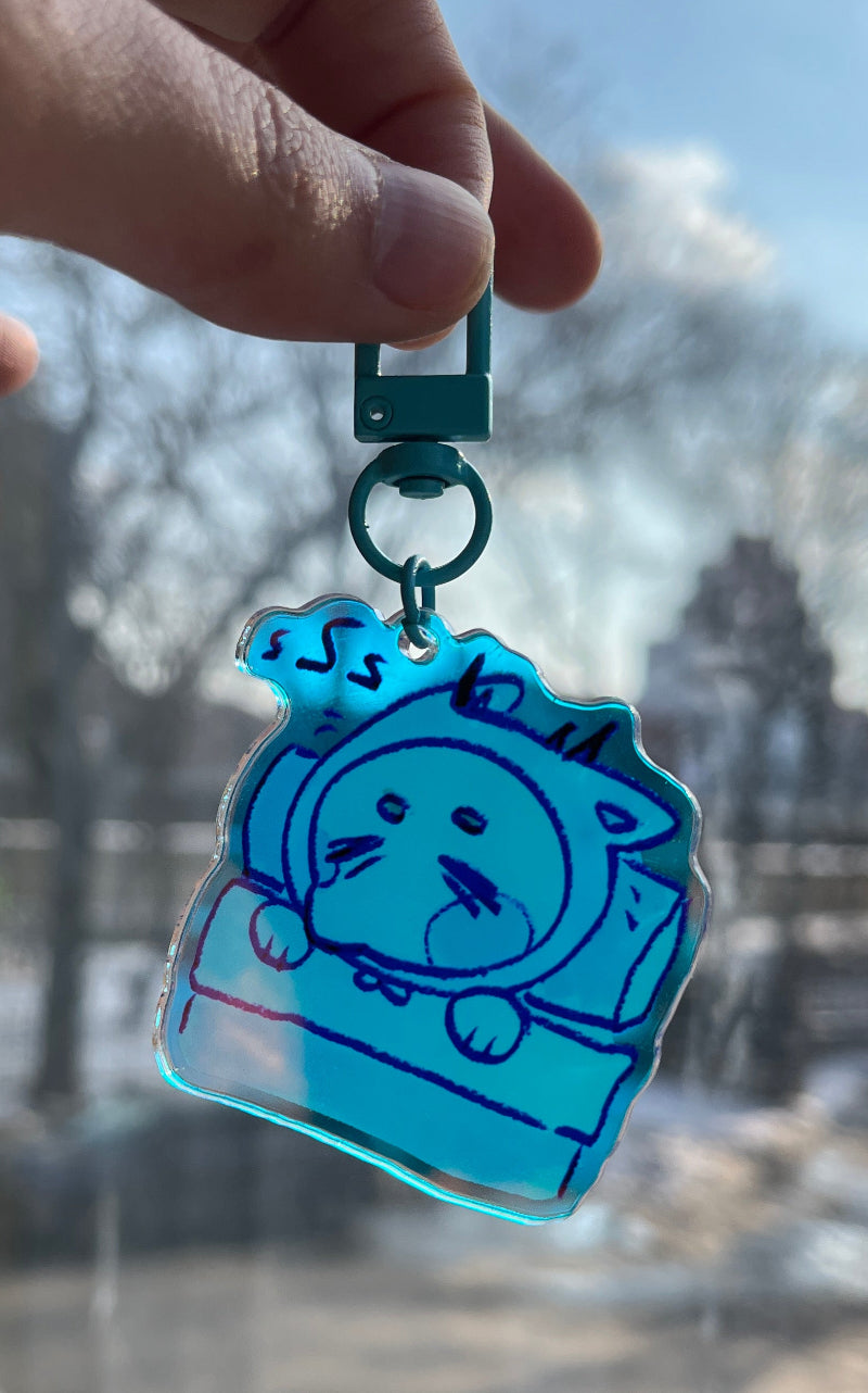 Hand holding a blue cartoon character keychain with a cityscape in the background