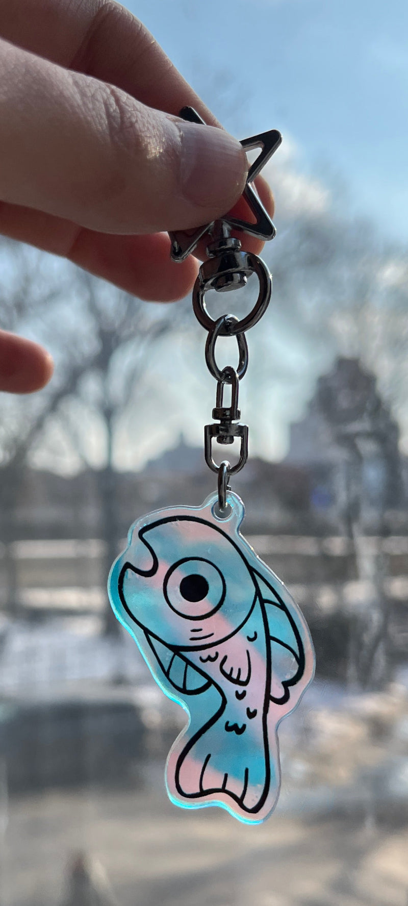 Hand holding a keychain with a fish design in front of a window