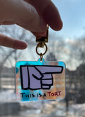 Keychain with a hand gesture design held by a hand against a blurred outdoor background