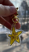 Hand holding a yellow star-shaped keychain with a blurred background of a street scene.