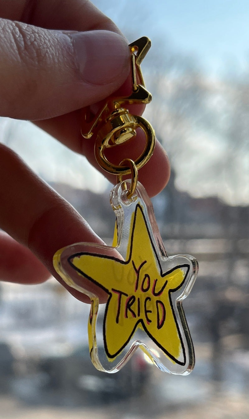 Hand holding a yellow star-shaped keychain with text, blurred background