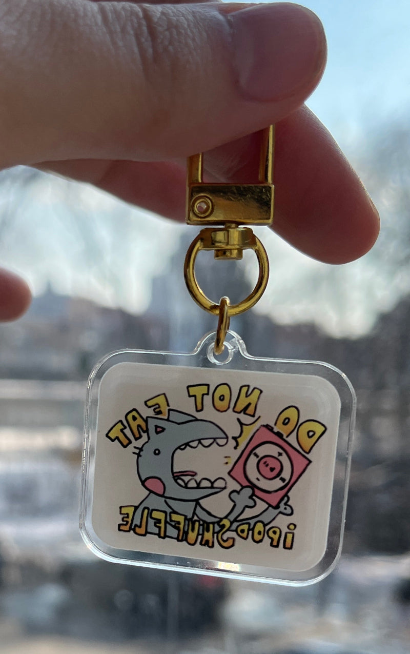 Hand holding a small keychain with cartoon character design against a blurred indoor background