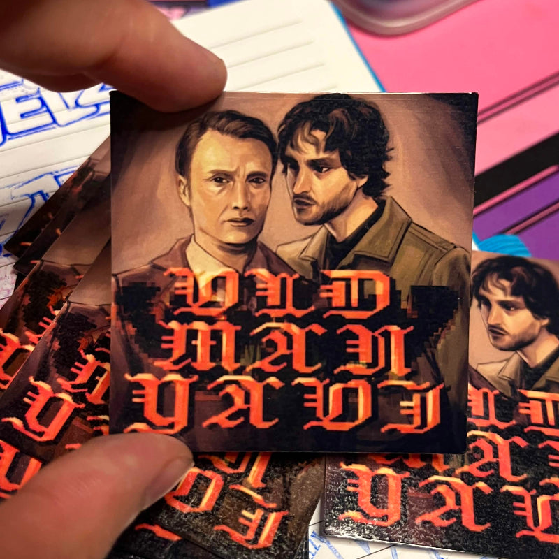 Small sticker with two portraits and stylized text held by a hand on a colorful background