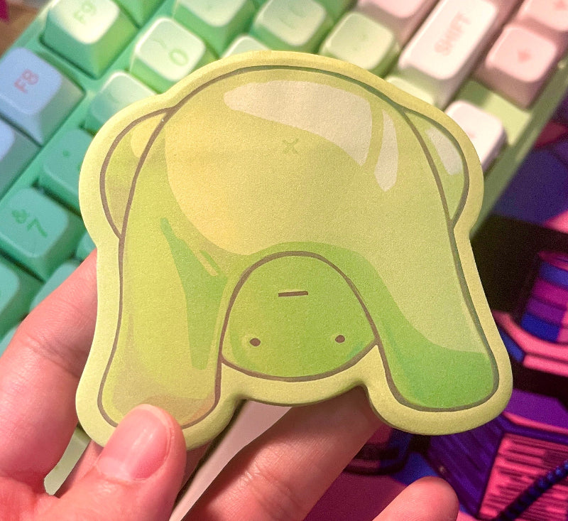 Hand holding a green sticky note pad over a colorful keyboard and mouse pad.